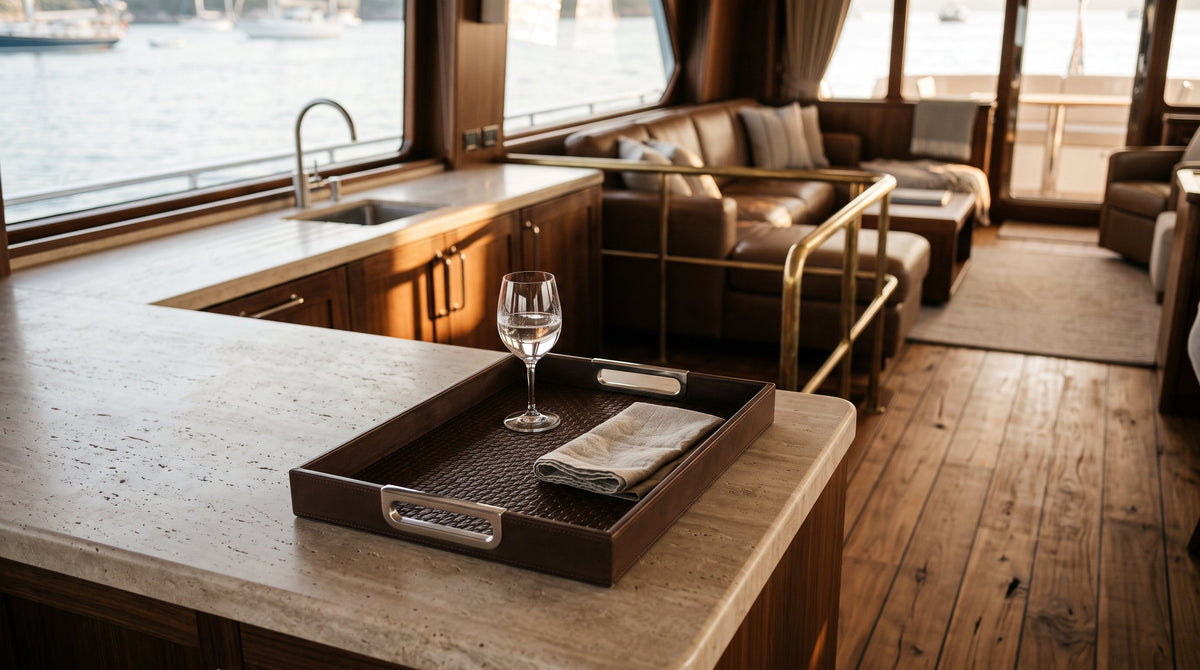 Woven-embossed leather serving tray with polished steel handles on a honed travertine counter in a yacht salon.