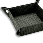 Corner of the 20 x 20 cm valet tray fastened with a polished metal press-stud, piping tracing the top edge of the woven leather