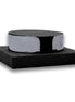 Black coaster stack in a polished steel band, seated on a square woven leather base