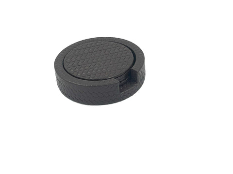 Round black leather coaster holder seen from above, a finger notch cut into the woven-embossed wall