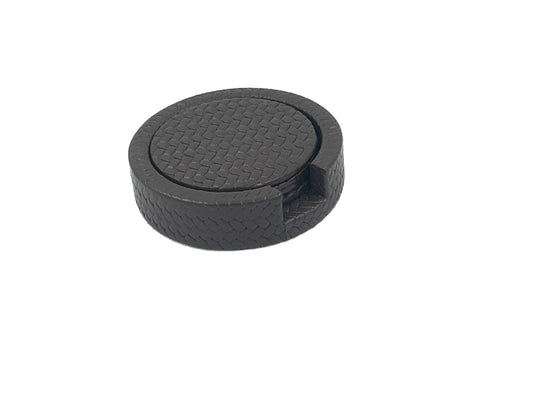 Round black leather coaster holder seen from above, a finger notch cut into the woven-embossed wall