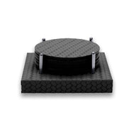 Six round black leather coasters stacked between four polished steel posts on a square woven-leather base