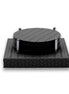 Six round black leather coasters stacked between four polished steel posts on a square woven-leather base