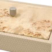Close above the corner, honeycomb-scaled leather turning the edge beside a burl lid and its knurled metal knob