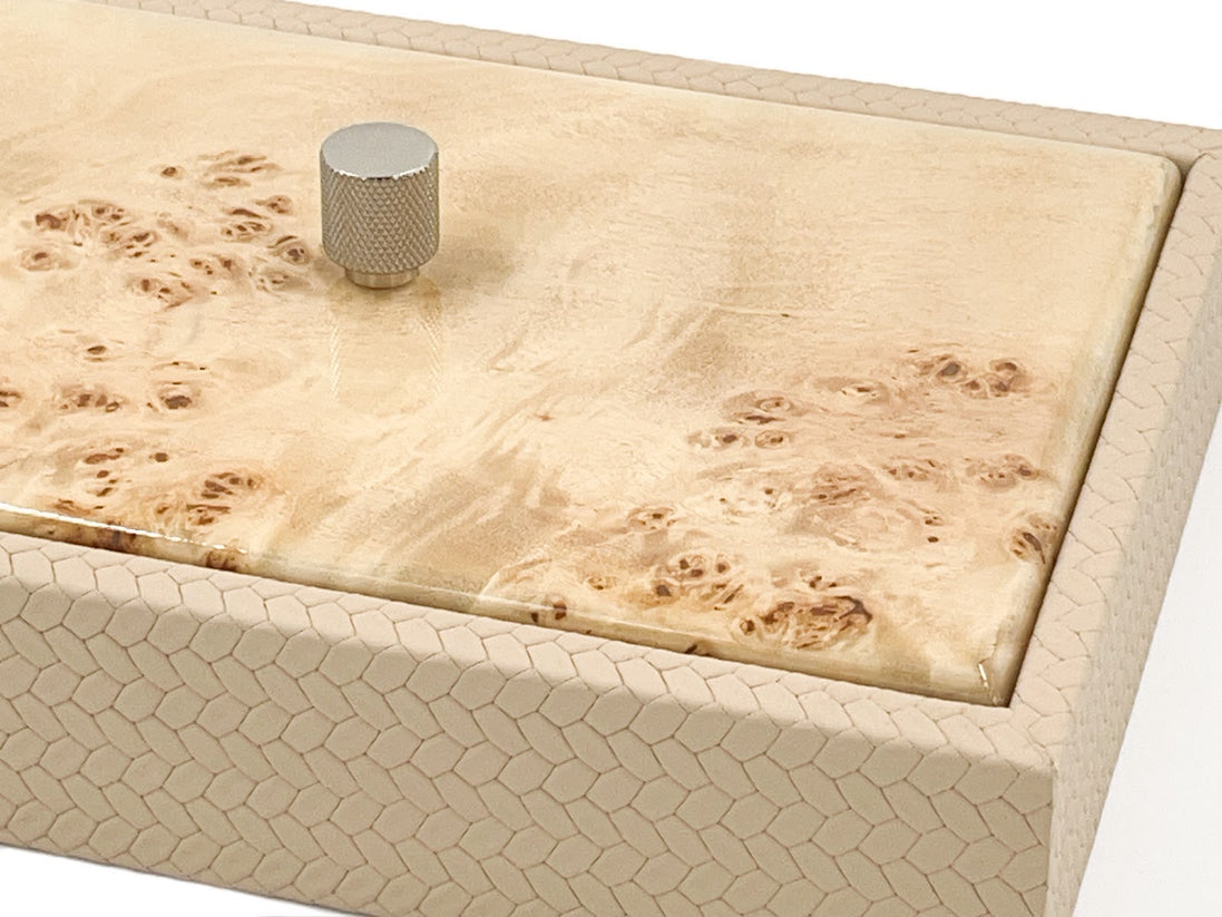 Close above the corner, honeycomb-scaled leather turning the edge beside a burl lid and its knurled metal knob
