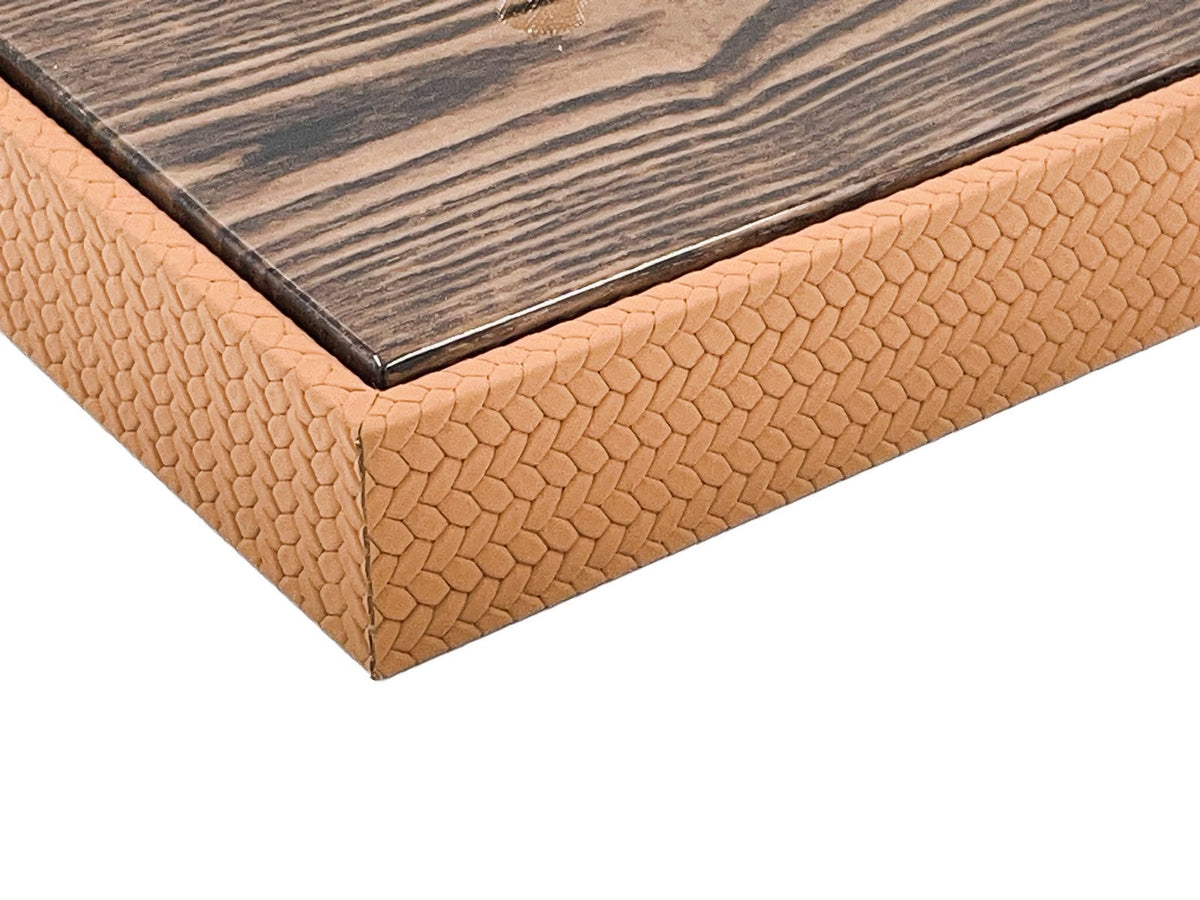 Close on the box corner, the lacquered mahogany lid edge above a mitred seam in the embossed leather