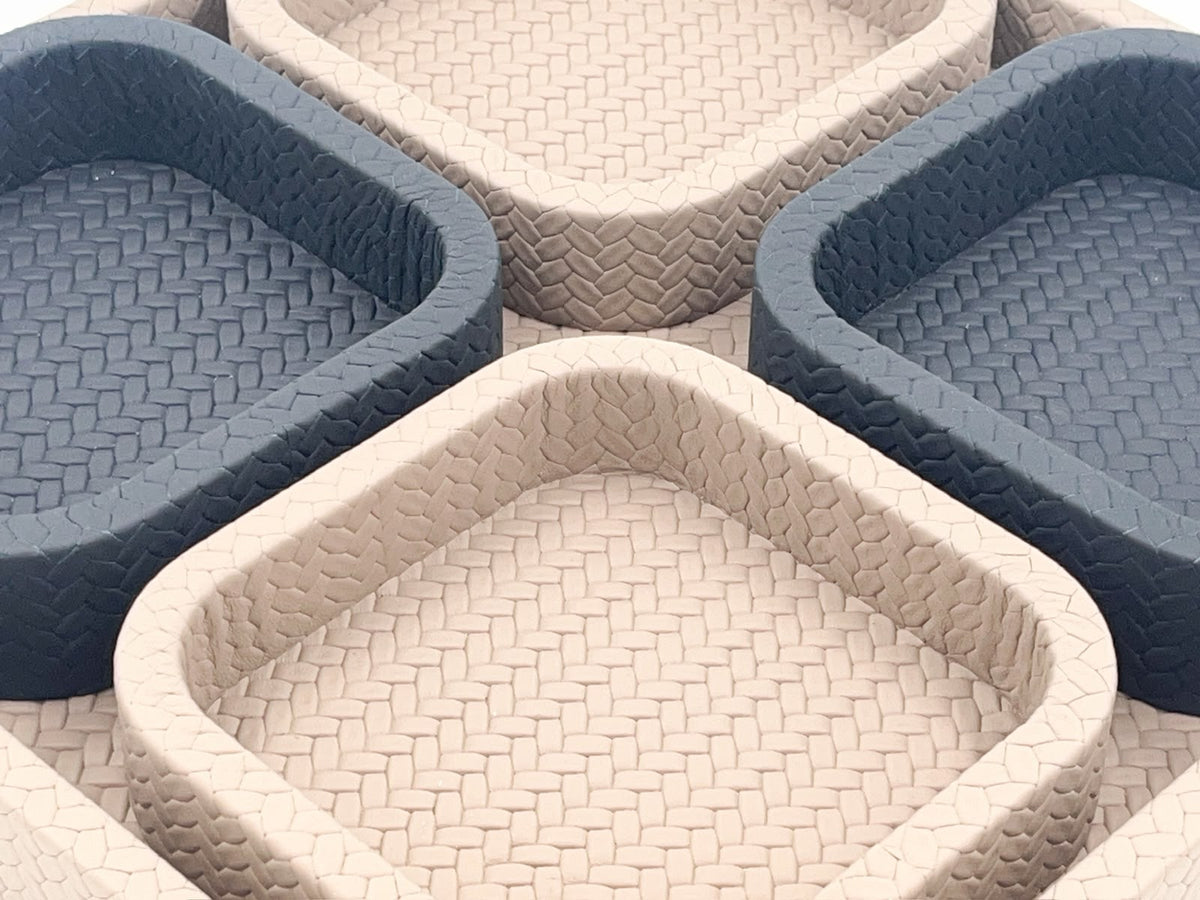 Close across the inner rims, a coarse plait on the darker trays against a finer weave on the pale leather ones