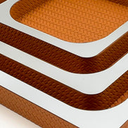Corner of the nested set, three mirror-polished rims stepping in over woven tan leather walls