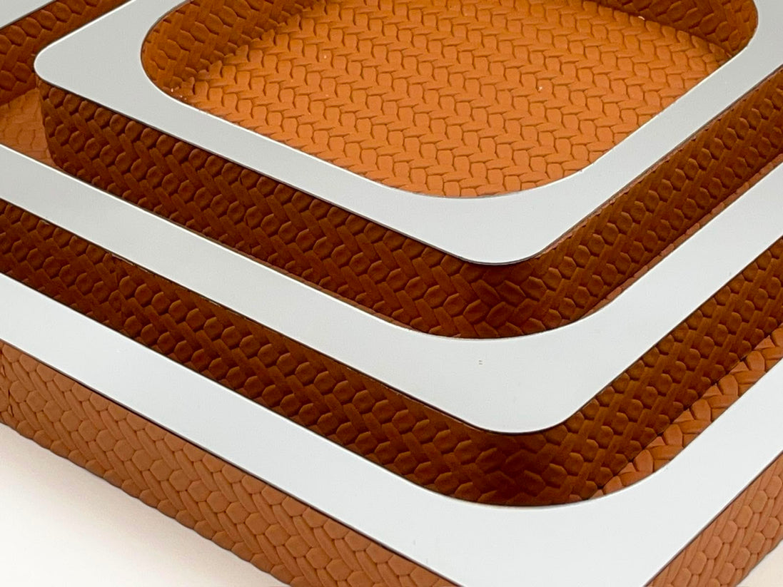 Corner of the nested set, three mirror-polished rims stepping in over woven tan leather walls