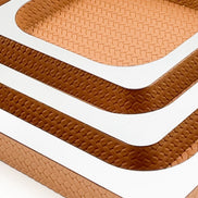 The same corner in a lighter leather, the polished rim of the 41 cm tray running out of frame below two smaller ones