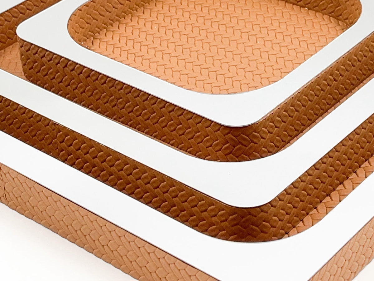 The same corner in a lighter leather, the polished rim of the 41 cm tray running out of frame below two smaller ones
