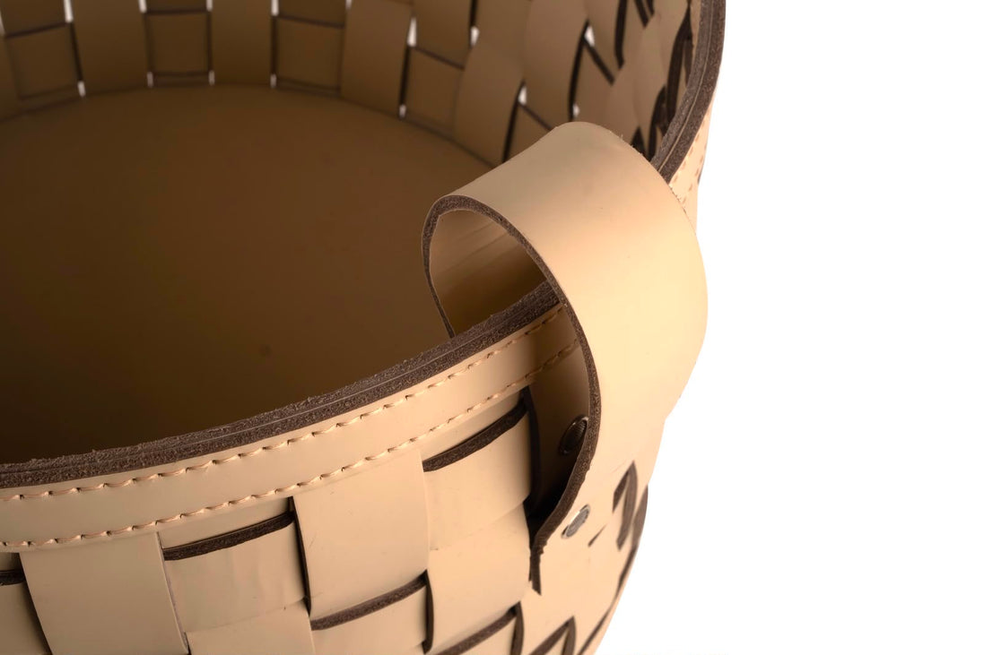 Close on a rolled leather handle, the strap end lapped and stitched over the basket's darker lining
