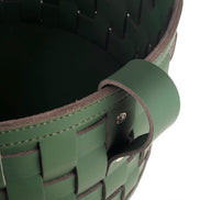 Close on the rim of the 24 cm deep basket, a folded leather handle riveted through the stitched binding above wide plaited straps