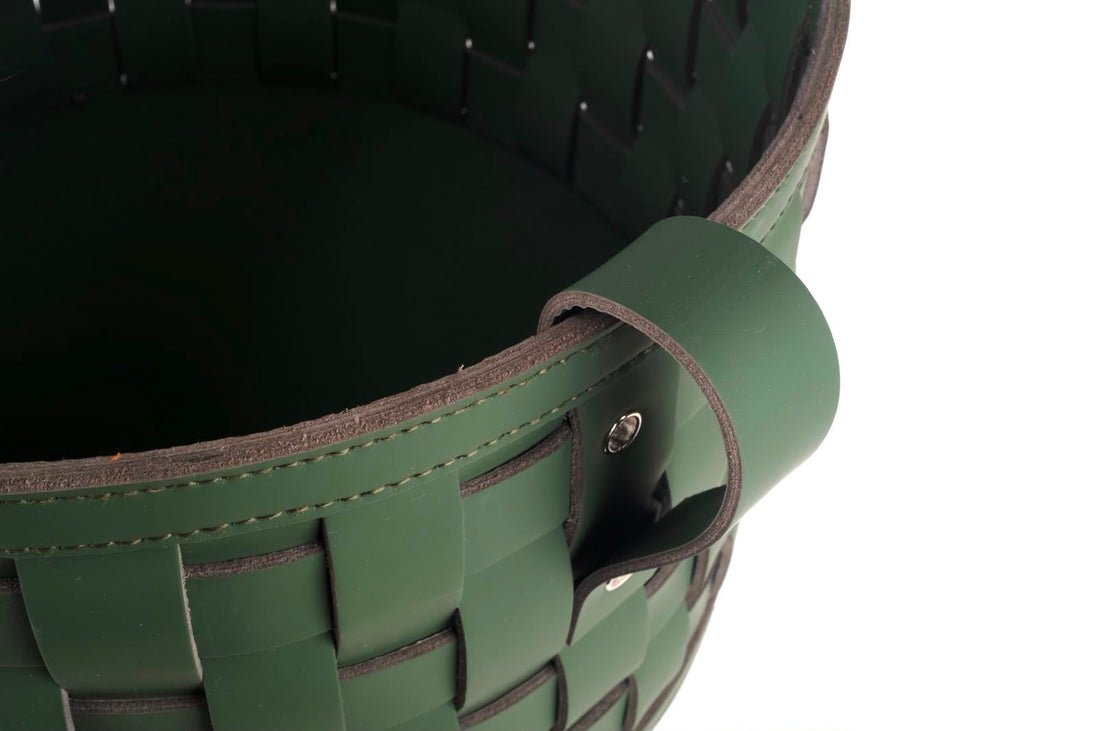 Close on the rim of the 24 cm deep basket, a folded leather handle riveted through the stitched binding above wide plaited straps