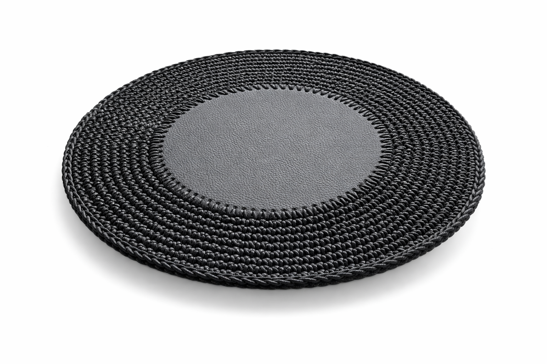 Black round placemat at an angle, the 1 cm crocheted border sitting flat around the leather centre