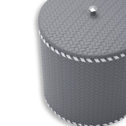 Close on the grey lid, faceted steel knob and woven-embossed leather at full scale above the laced rim