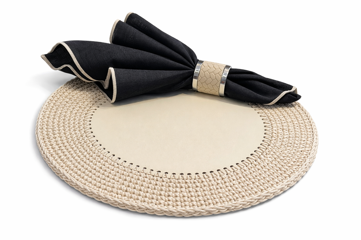 Cream round placemat, leather centre bare, black napkin resting on the raised cord border