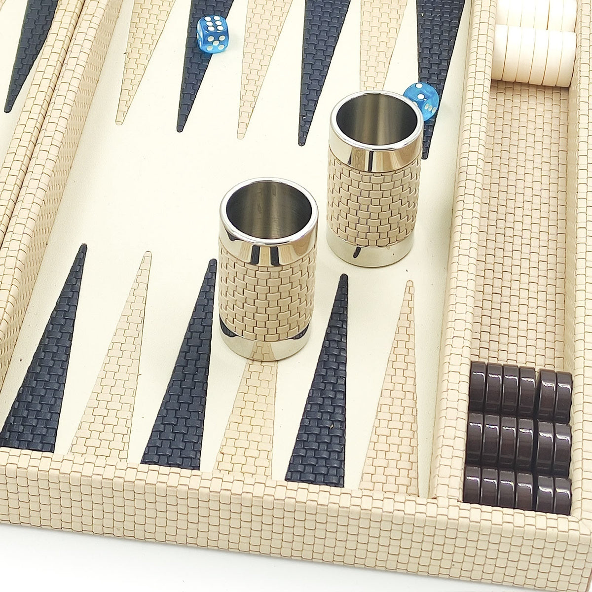 Close-up of cream basket-weave leather dice cups with polished metal rims beside navy woven points