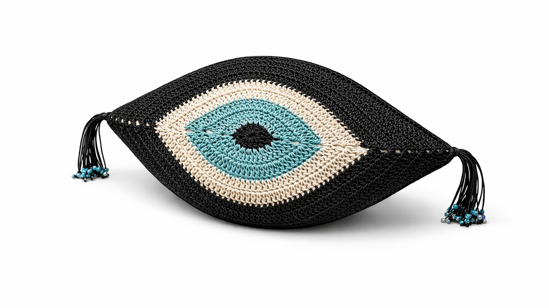 The black evil eye cushion at an angle, cream ring around the turquoise iris