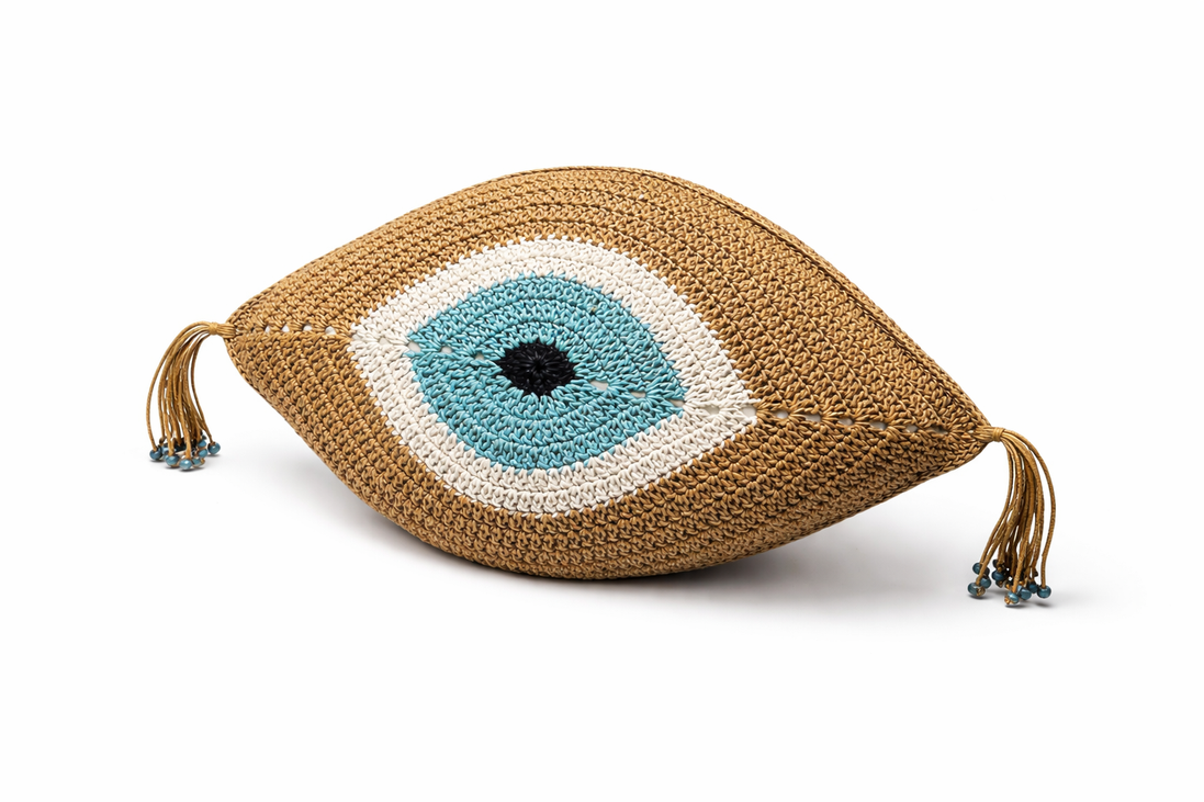 The camel evil eye cushion at an angle, crocheted rings around the iris